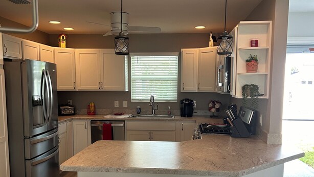 A modern kitchen with a central island, stainless steel appliances, and pendant lighting. - Charming 2-bedroom house in fabulous Hawkins Village of The Villages Florida. (Wildwood)