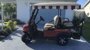 A red and white golf cart parked in a driveway. - Charming 2-bedroom house in fabulous Hawkins Village of The Villages Florida. (Wildwood)