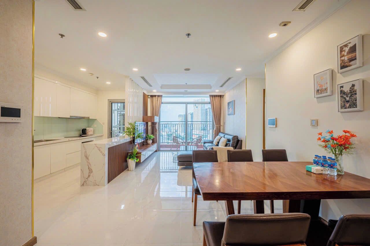 A modern kitchen with a marble countertop, a dining area with a wooden table and chairs, and a balcony with a view of the city.