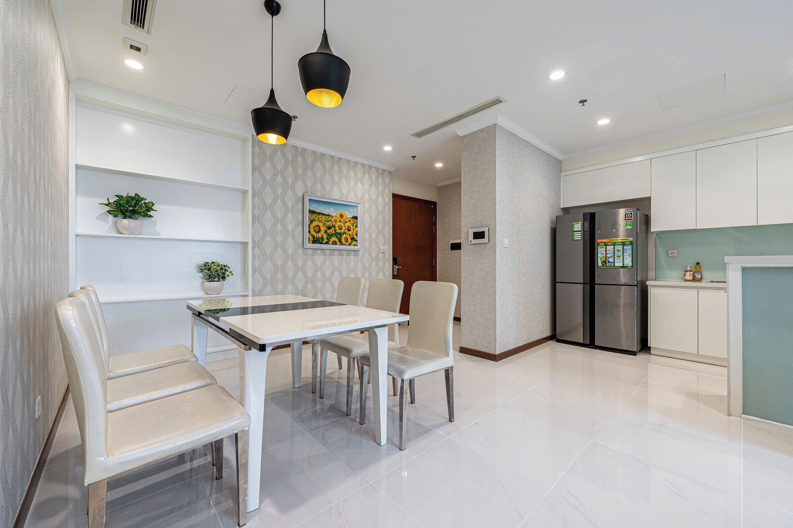 A modern kitchen with white cabinets, a stainless steel refrigerator, and a dining area with a white table and chairs.