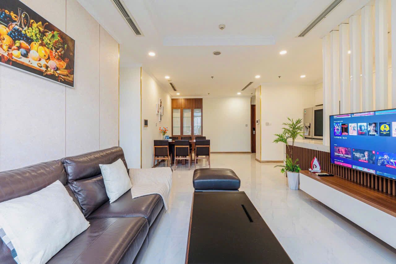 A modern hotel lobby with a leather sofa, a reception desk, a dining area, and a large TV screen.