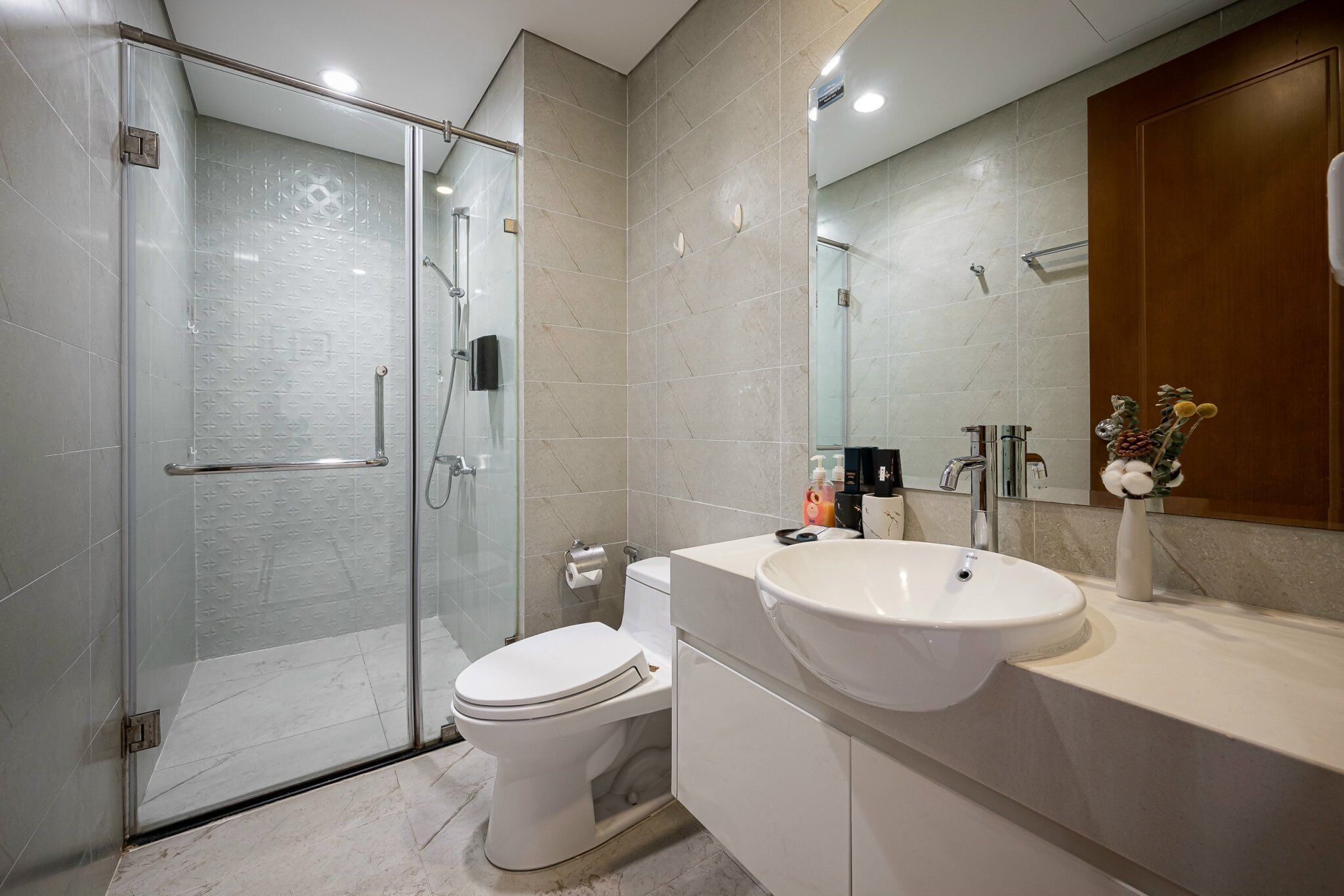 A modern bathroom with a glass-enclosed shower, a white toilet, and a vanity with a sink and mirror.
