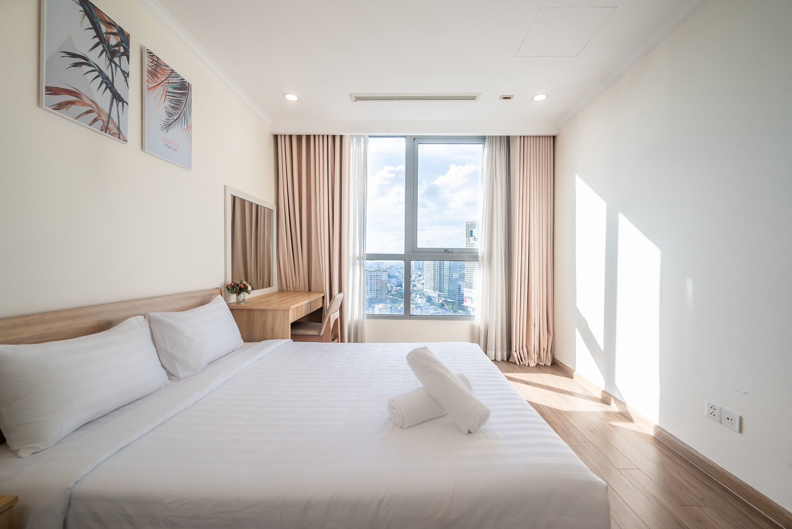 A hotel room with a large bed, a desk, and a view of the city through a large window.