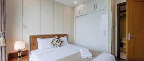A hotel room with a bed, bedside table, lamp, wardrobe, and a door leading to a bathroom.