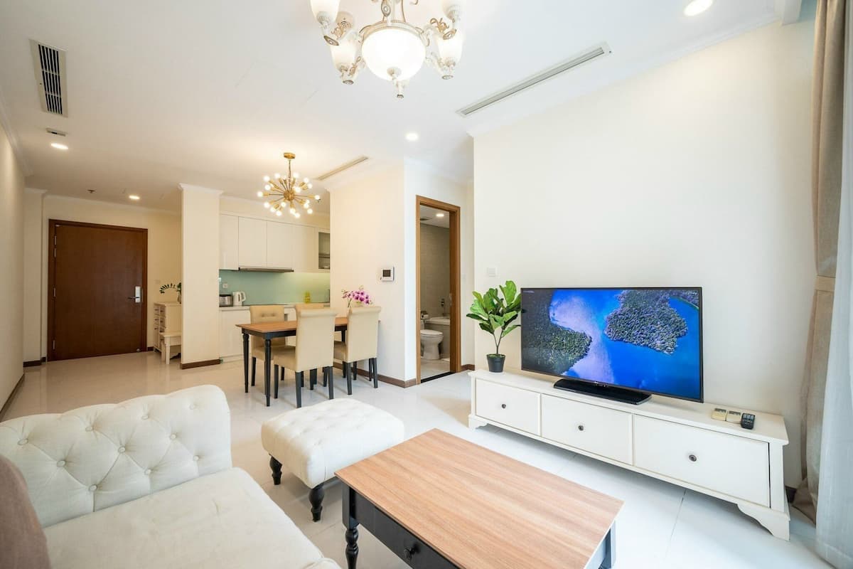 Uma sala de estar moderna com televisão, uma área de refeições e uma cozinha ao fundo.