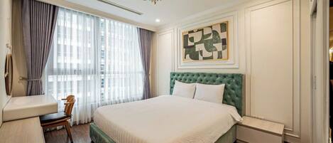 A hotel room with a green upholstered bed, a bedside table, a chair, and a large window with curtains.