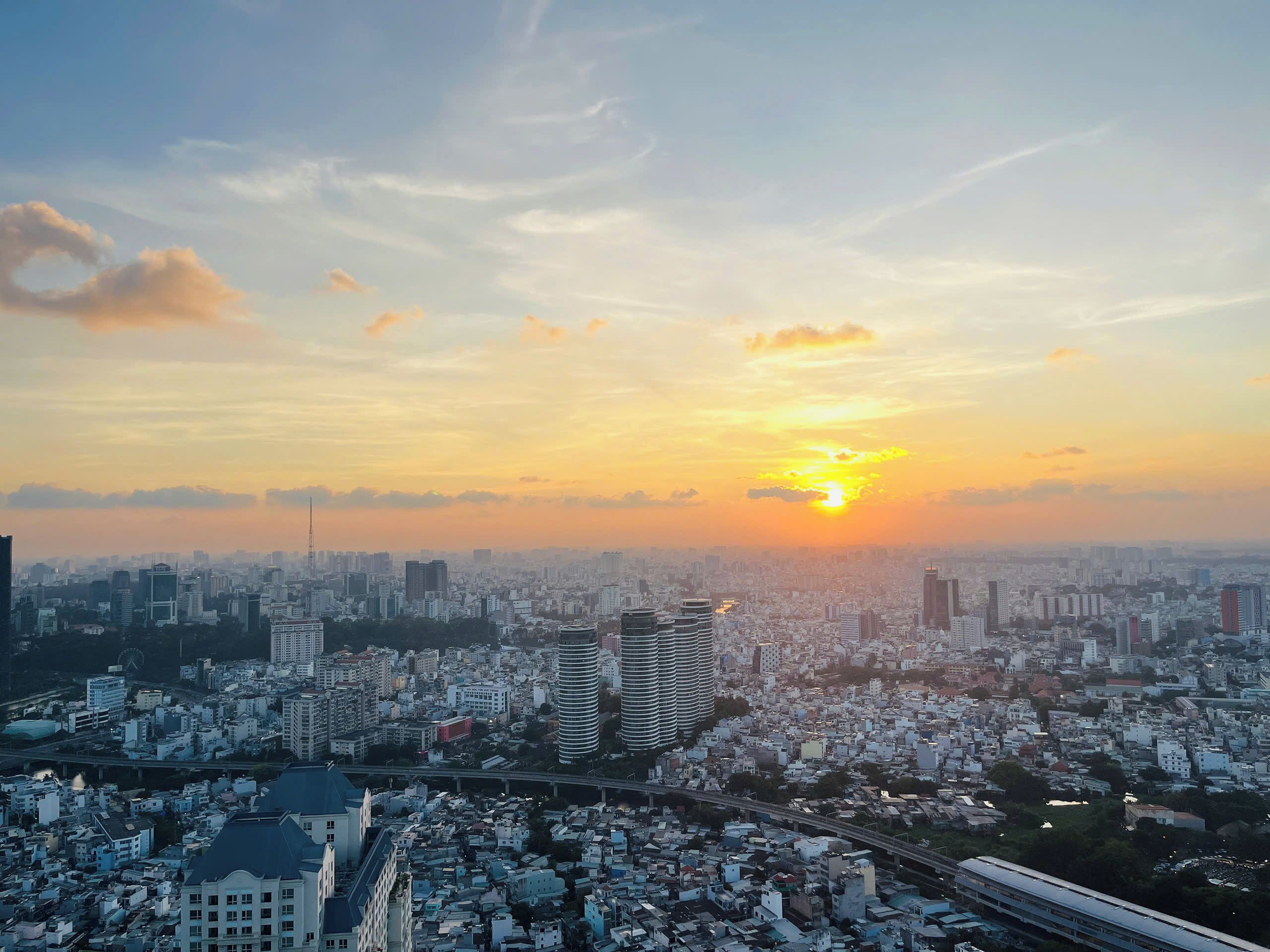 Une vue urbaine avec un coucher de soleil, des bâtiments et une voie ferrée surélevée.