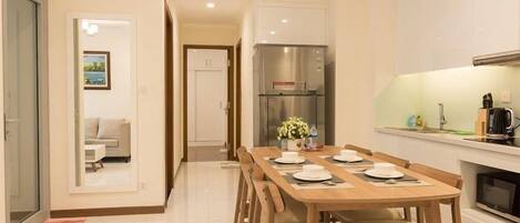 A modern kitchen with a dining area, featuring a stainless steel refrigerator, a built-in oven, and a dining table set for four.