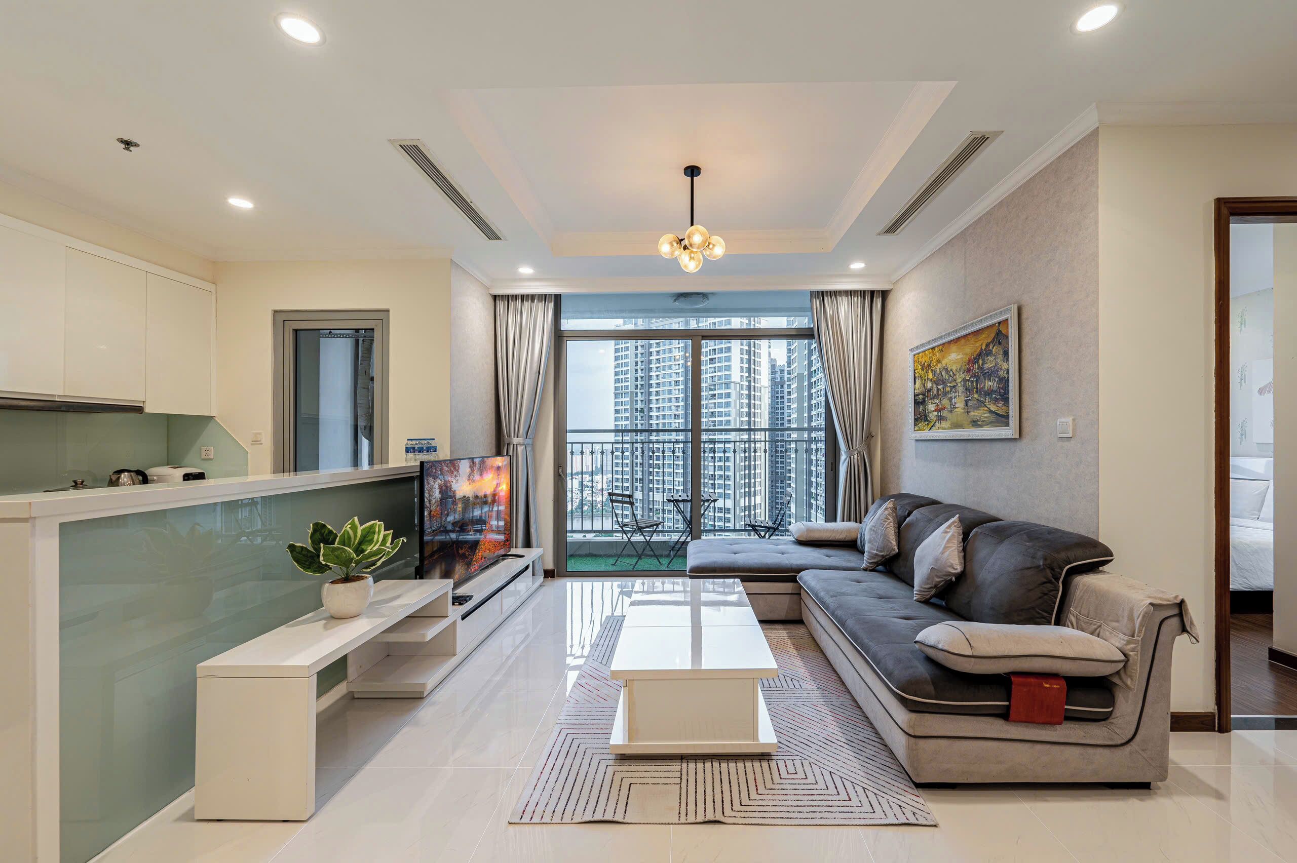 A modern living room with a sofa, coffee table, TV, and a balcony with a city view.