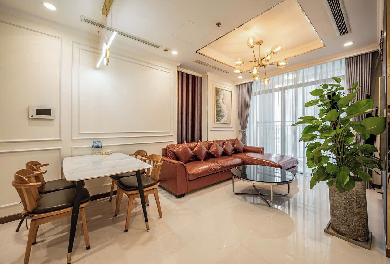 A modern living room with a brown leather sofa, a glass coffee table, a dining table with chairs, and a large potted plant.