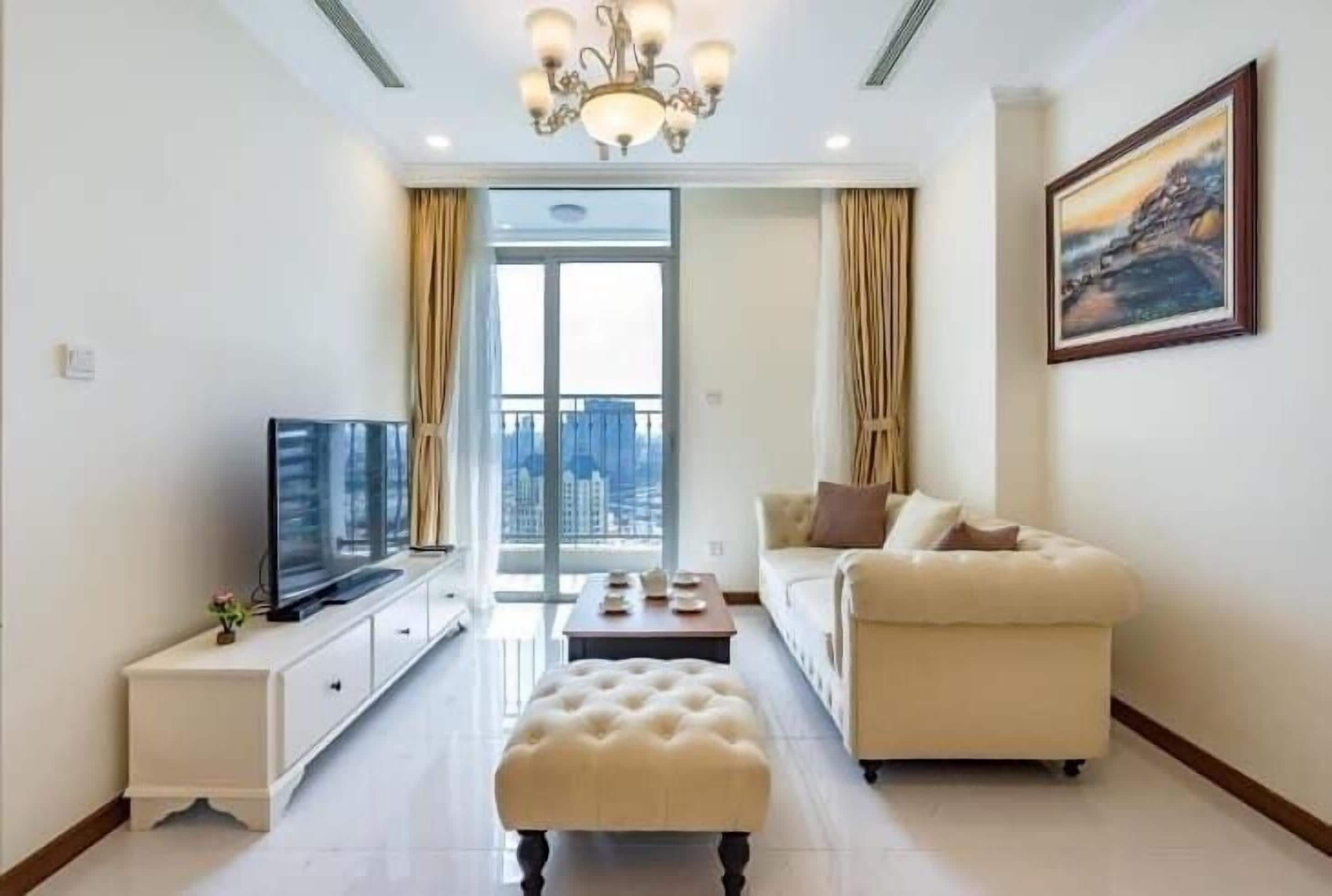 Una sala de estar moderna con un televisor de pantalla plana, un sofá color crema, una mesa de centro y un amplio ventanal con cortinas.