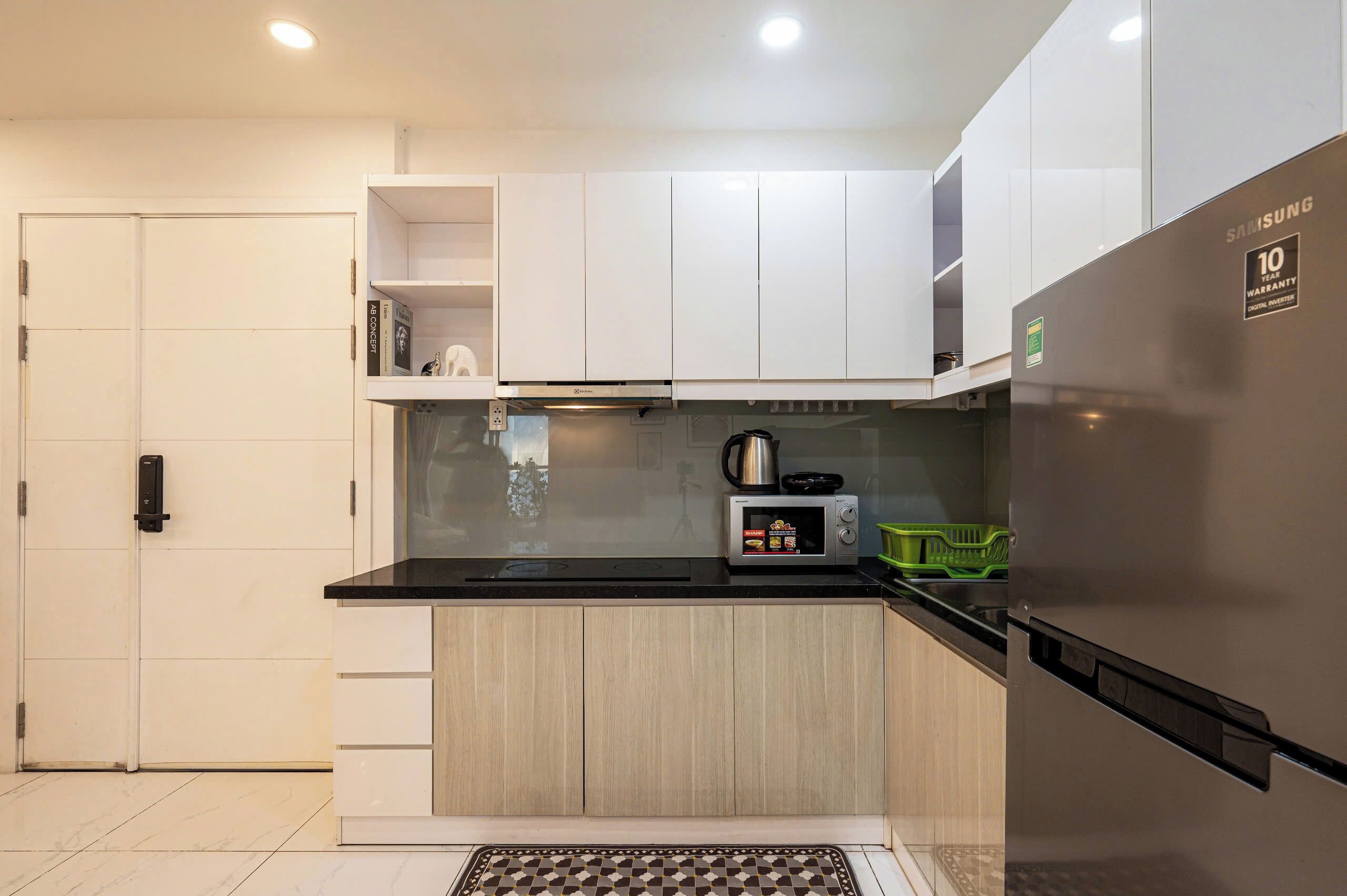 A modern kitchen with white cabinets, a stainless steel refrigerator, a microwave, and a kettle.