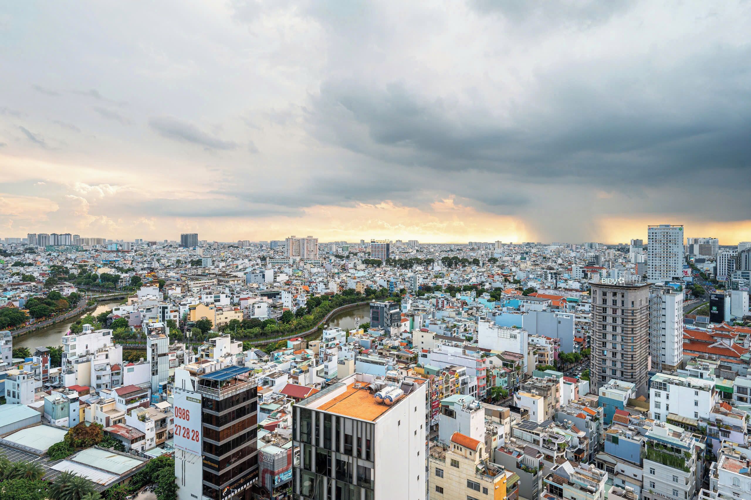 A densely packed urban cityscape with a river running through it, numerous buildings, and a cloudy sky.