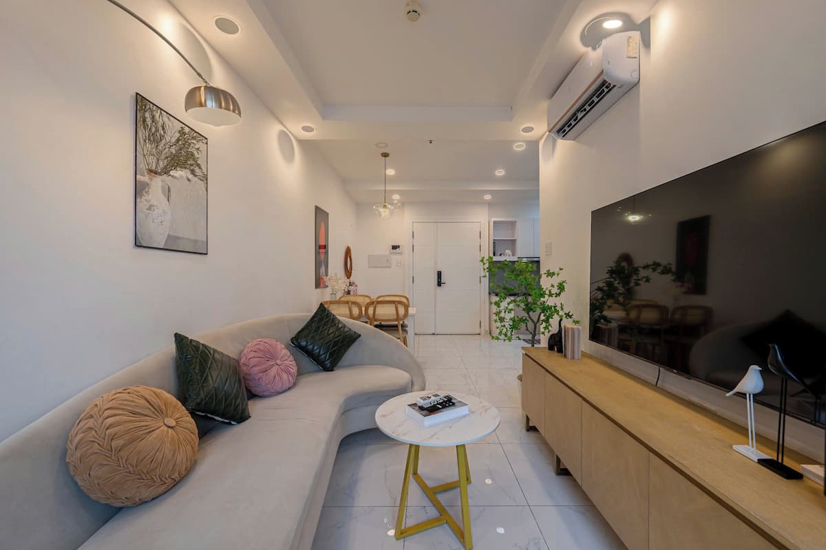Uma sala de estar moderna com um sofá, uma mesa de centro, uma televisão e uma área de jantar ao fundo.