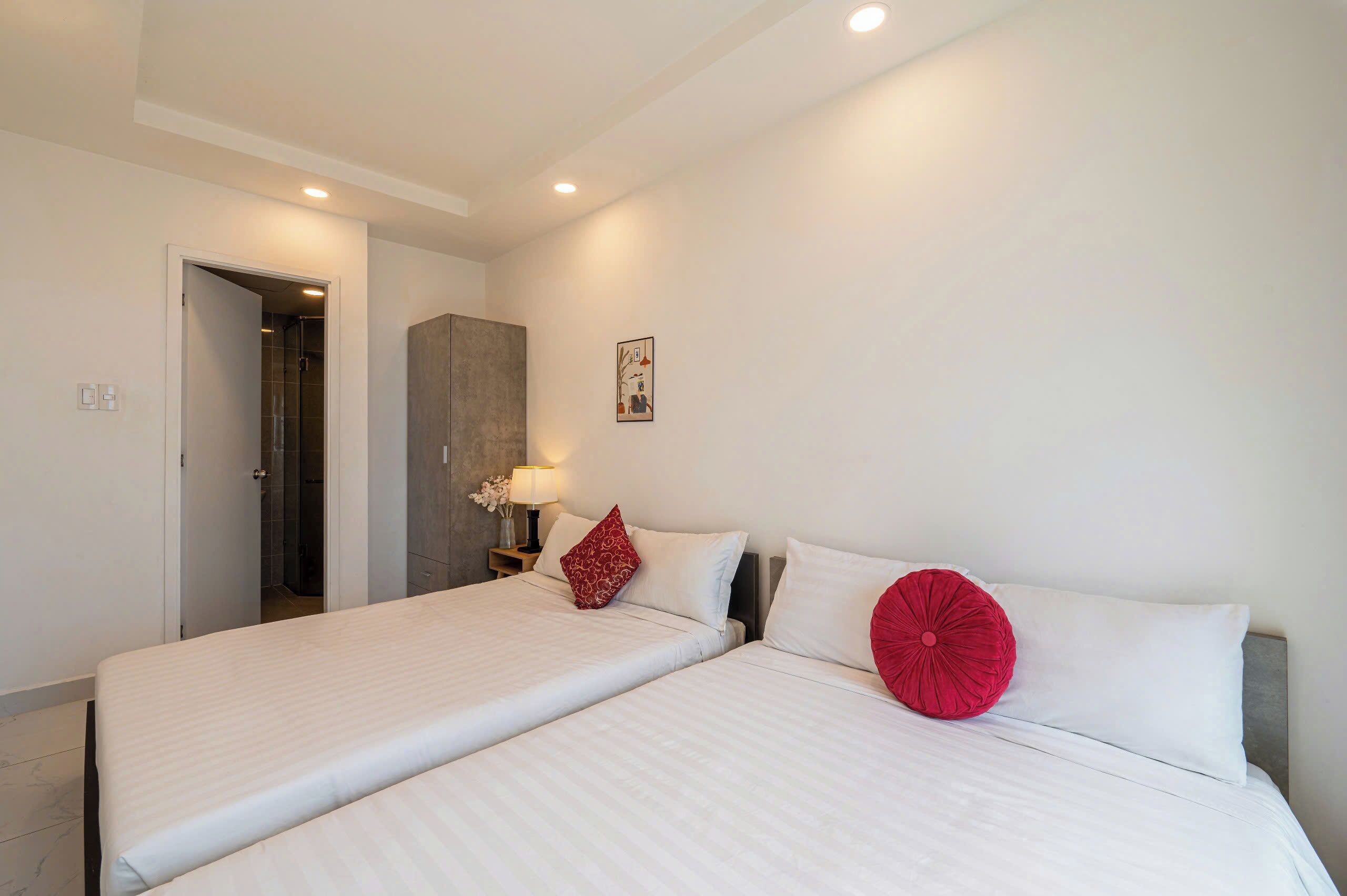 A hotel room with two beds, a nightstand with a lamp, and a door leading to a bathroom.