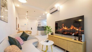 Een moderne woonkamer met een grote flatscreen televisie, een bank met decoratieve kussens, een klein rond salontafeltje en een houten kast.