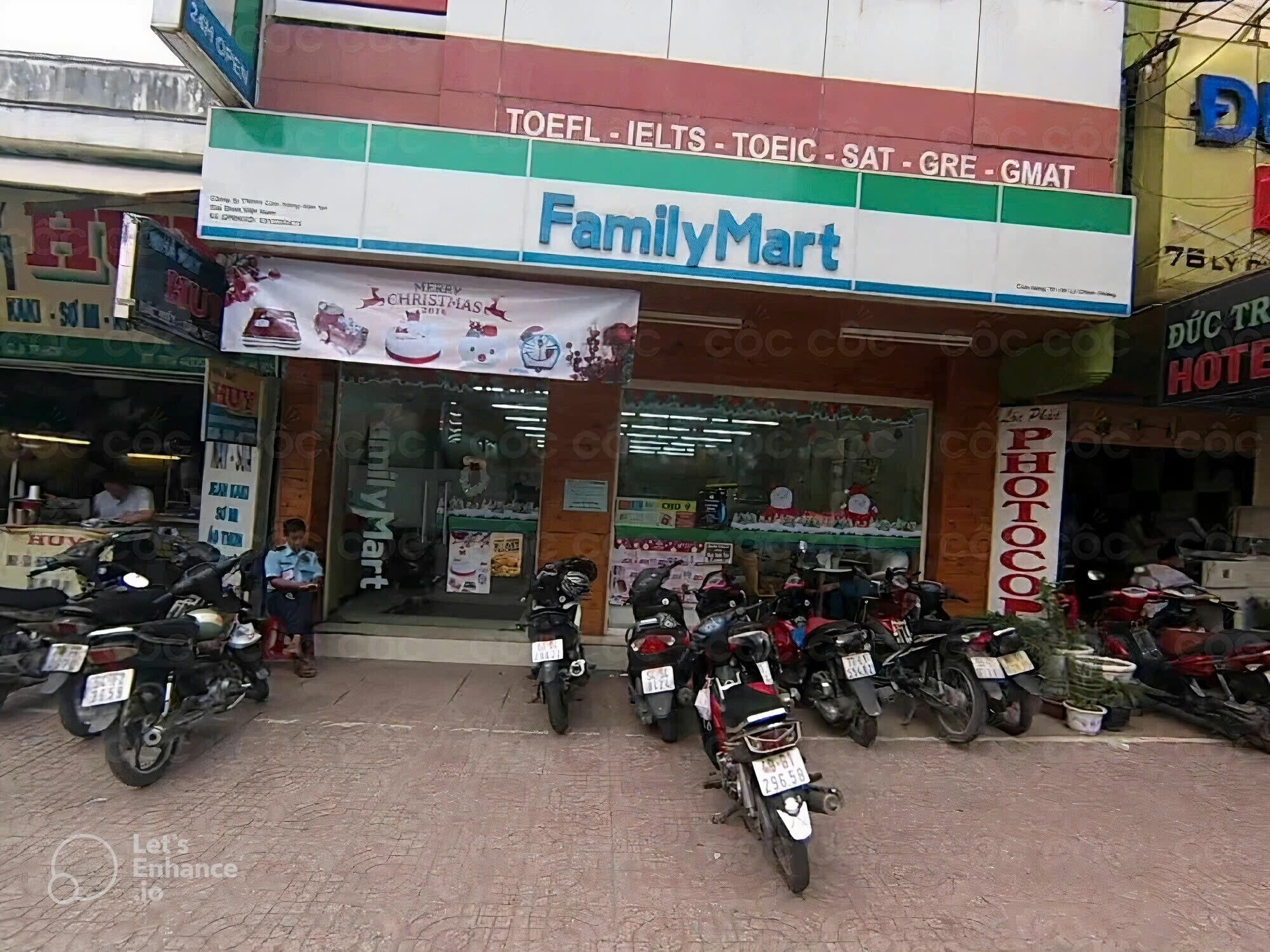 Una tienda FamilyMart con un cartel publicitario de TOEFL, IELTS, TOEIC, SAT, GRE, GMAT y un banner navideño.