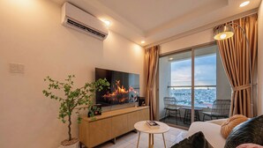 Een moderne woonkamer met een flatscreen-televisie, een potplant, een bank en een balkon met uitzicht over de stad.