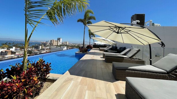 Un espace piscine aménagé sur le toit, avec des chaises longues et des parasols, offrant une vue sur le paysage urbain.