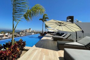 Un espace piscine aménagé sur le toit, avec des chaises longues et des parasols, offrant une vue sur le paysage urbain.