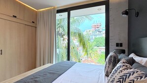 Une chambre moderne avec un grand lit, une vue sur le paysage urbain à travers une porte-fenêtre coulissante et une armoire en bois.