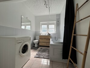 Une petite salle de bain équipée d’un lave-linge, de toilettes, d’un lavabo et d’une fenêtre.