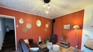 A living room with a fireplace, a sofa, a lamp, and decorative wall hangings. - L'escale de Saint Martin (Saint-Martin-de-Mailloc)