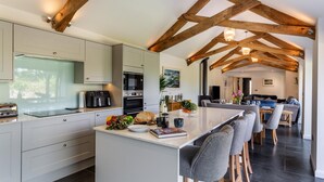 A modern kitchen with a large island, wooden beams, and a dining area with bar stools. - 3 Bed in Hartland (oc-w29797) (Hartland)