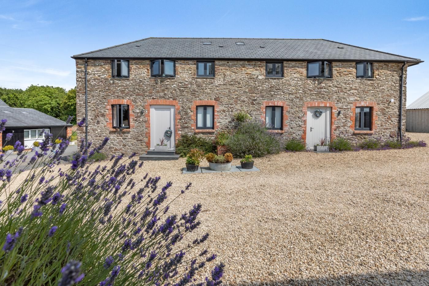 A stone building with multiple doors and windows, surrounded by gravel and lavender plants.