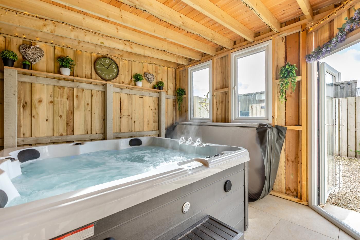 Een hottub in een houten hut met ramen en potplanten.