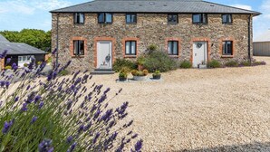 Un edificio in pietra con vialetto sterrato e piante di lavanda.