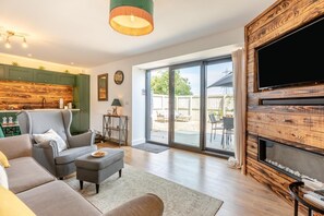 A modern living room with a sofa, a coffee table, and a fireplace. There is a large window and a sliding glass door leading to a patio. - 2 Bed in Harracott (oc-m29831) (Harracott)