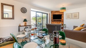 Un soggiorno moderno con un tavolo da pranzo in vetro, sedie verdi, un divano e una TV montata su una parete in legno.