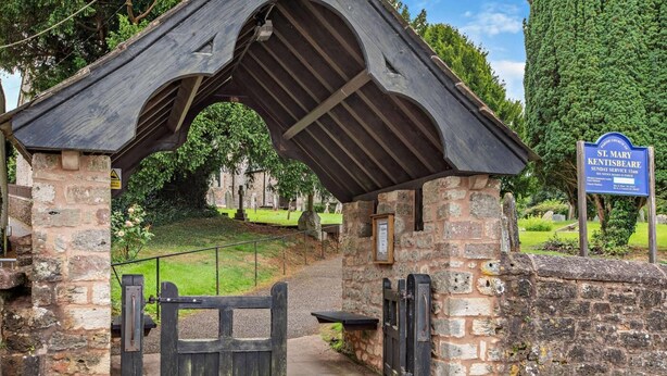 A stone structure with a wooden roof, a gate, and a sign indicating a Sunday service.