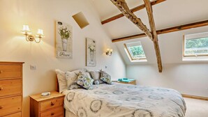 A bedroom with a sloped ceiling, a wooden dresser, a bed with floral bedding, wall-mounted lights, and framed artwork.
