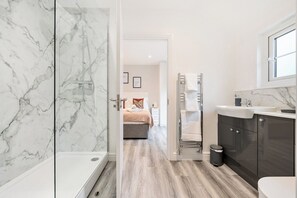 Ein modernes Badezimmer mit Dusche, Toilette und Waschbecken. Im Hintergrund ist ein Bett zu sehen.