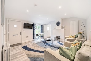 A modern living room with a sofa, a coffee table, and a TV mounted on the wall. - Wokingham - 1 Bedroom Cottage - Parking (Wokingham)