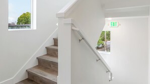 Una escalera con escalones de madera y paredes blancas, que lleva a una salida.