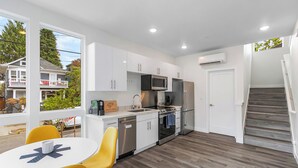 Una cocina moderna con armarios blancos, electrodomésticos de acero inoxidable y una zona de comedor con sillas amarillas.