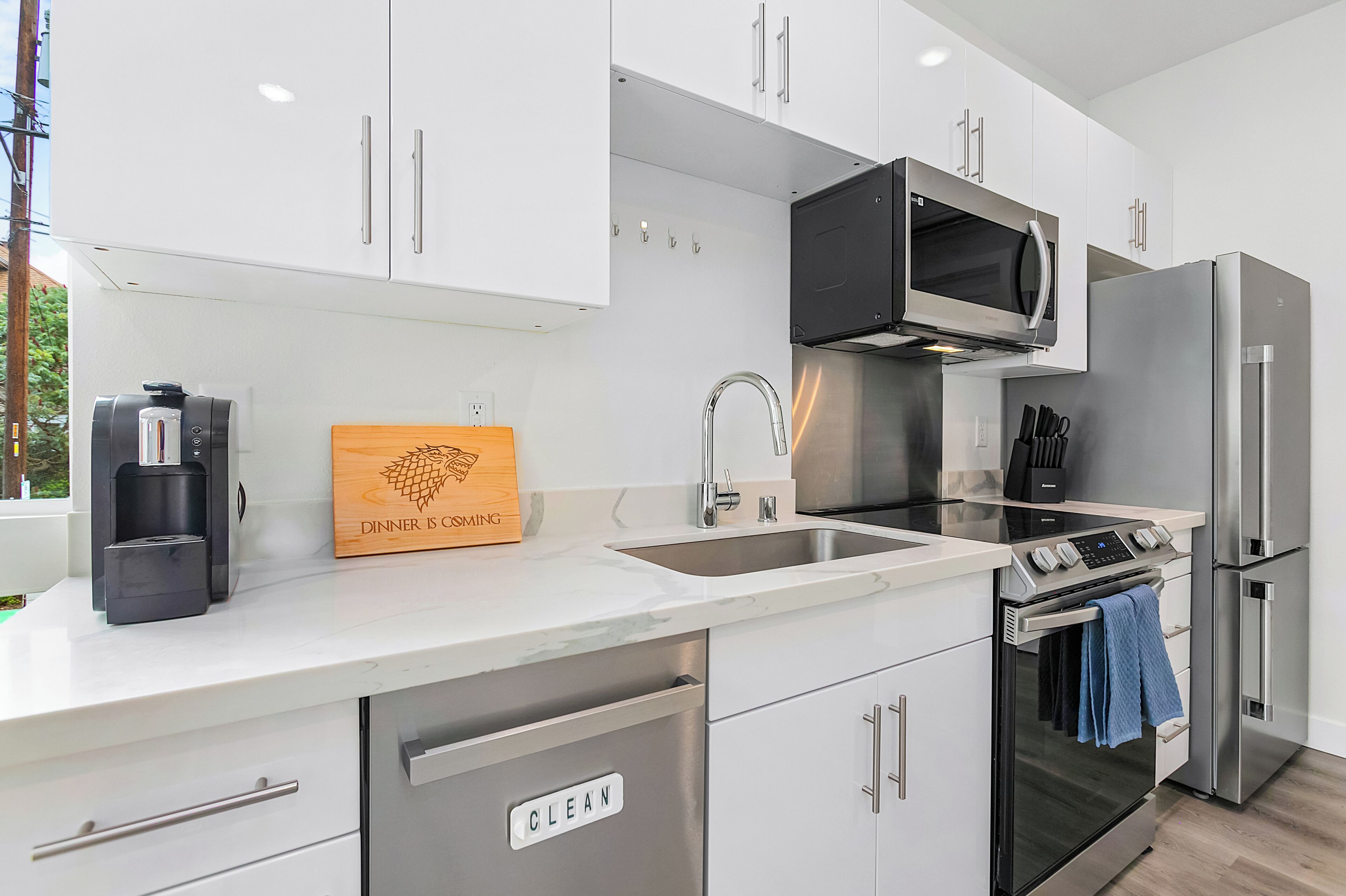 A modern kitchen with white cabinets, stainless steel appliances, a built-in microwave, and a coffee maker.
