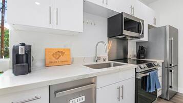 A modern kitchen with white cabinets, stainless steel appliances, a built-in microwave, and a coffee maker.