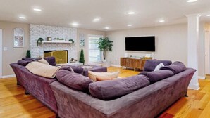 A spacious living room with a large sectional sofa, a flat-screen TV, and a fireplace. - Charming 3-bed, 2- bath house with open concept living and sunroom in Savannah (Savannah)