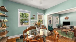 A dining area with a glass table and wooden chairs, a television in the living room, and a dartboard on the wall. - Charming 2 BR house in Old Hickory Village, a short walk from the lake road  (Nashville)