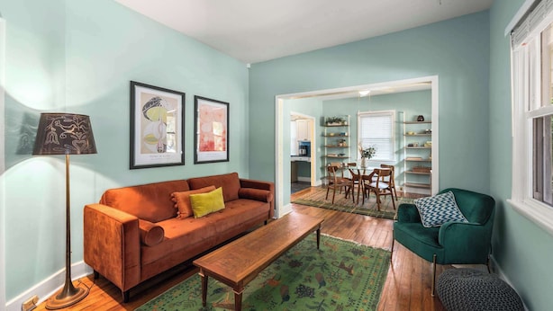 A living room with a sofa, a coffee table, a floor lamp, and a green armchair. There is a dining area with a table and chairs visible through an open doorway. - Charming 2 BR house in Old Hickory Village, a short walk from the lake road  (Nashville)