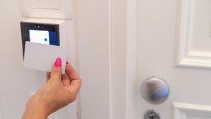 Mão segurando um cartão em frente a uma porta com fechadura digital e fechadura.