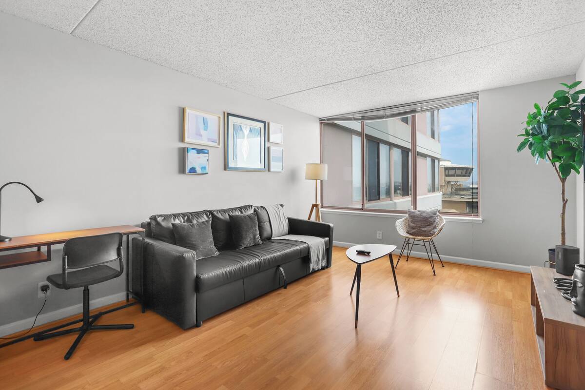 Una sala de estar moderna con un sofá de cuero, un escritorio de madera y un amplio ventanal con vistas a un edificio.