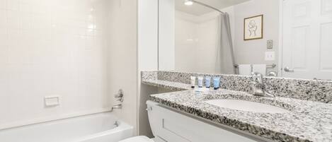 Un baño moderno con una bañera blanca, un inodoro, un lavabo de encimera de granito y un espejo grande.