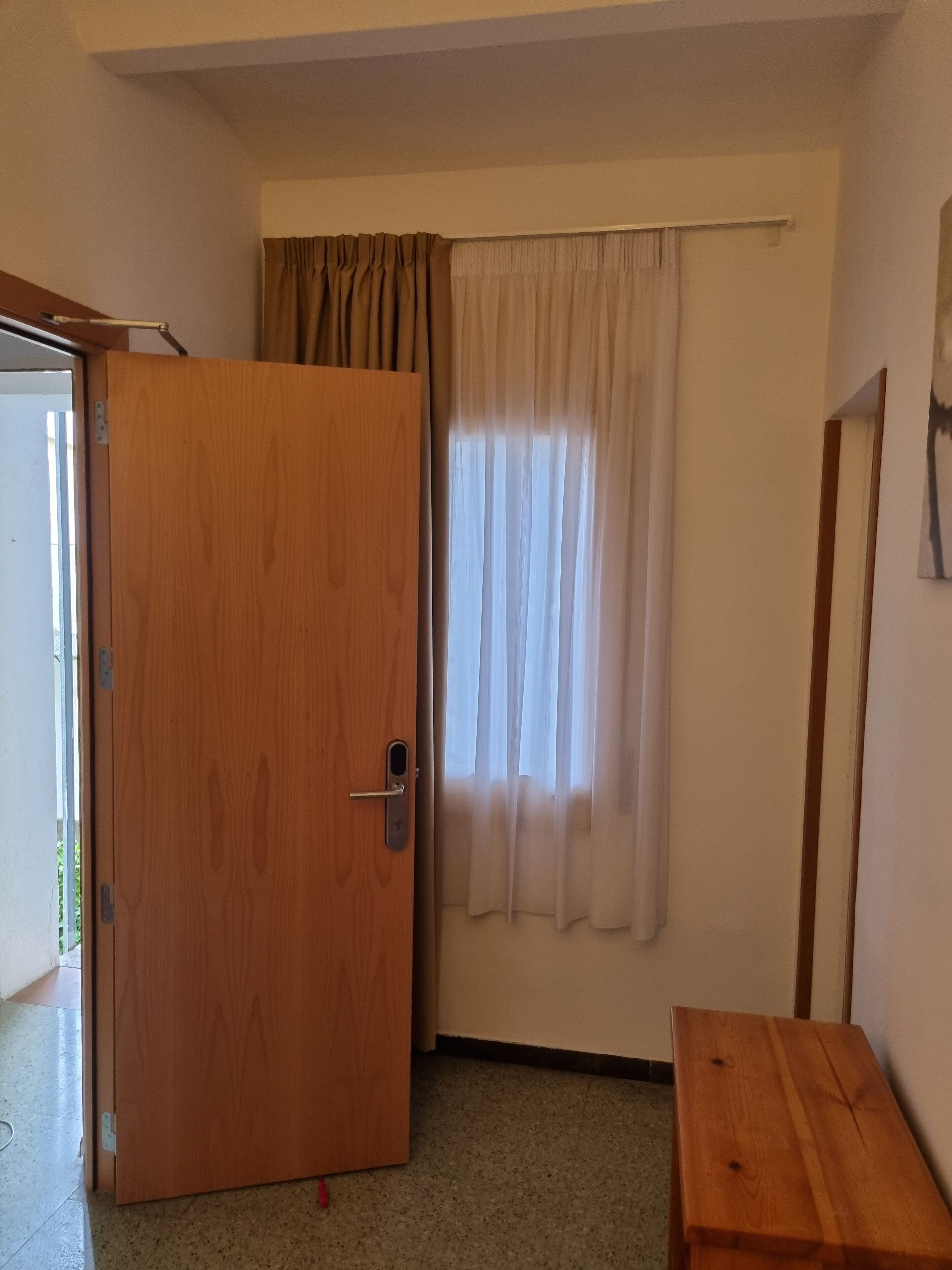 Une pièce avec une porte en bois, une fenêtre avec des rideaux et une petite table en bois.
