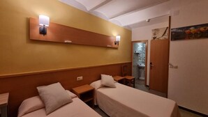 Ein Hotelzimmer mit zwei Einzelbetten, einem Holzkopfstück, einer Wandleuchte und einer Tür zu einem Badezimmer.