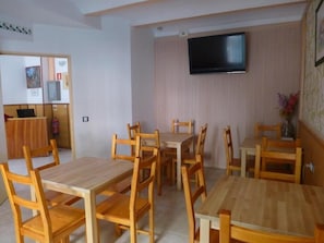 A dining area with wooden tables and chairs, a flat-screen TV mounted on the wall, and a small decorative plant on the right. - Pension El Ciervo (Lloret de Mar)